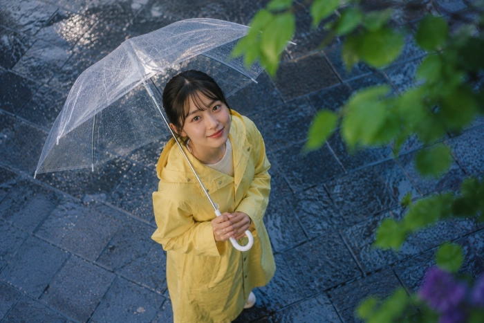 ・見出し『まとめ』に合う画像を作成してください・アイキャッチと同じ女性。雨が降っている。少し上から女性を見ている。女性は空(カメラ目線)を見て微笑んでいる・画像内に文字、ロゴ、透かしは入れない・商業用ブログ記事に使用するため、完全にオリジナルで著作権侵害のない構図にしてください。雨の中で透明な傘を差した若い女性が、空を見上げながら穏やかに微笑んでいる。濡れた石畳や木々の緑が雨に映え、雨の日の心地よさや前向きな気持ちが伝わる温かな風景。