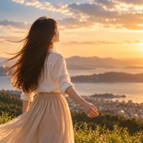 夕日を見つめながら風を感じる女性と海を望む風景